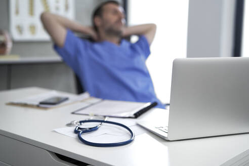 Laptop auf dem Schreibtisch mit einem entspannenden Arzt im Hintergrund - ABIF01907