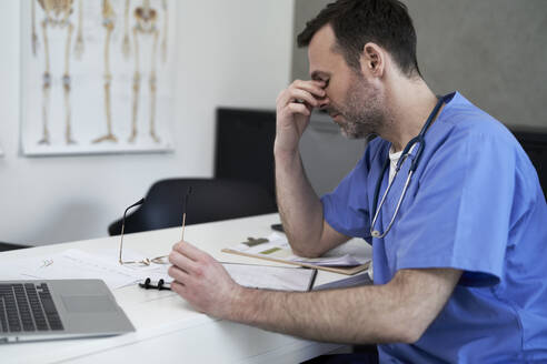 Müder Arzt sitzt am Schreibtisch in der Klinik - ABIF01908