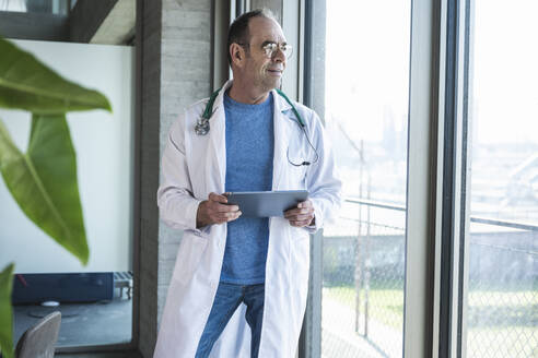 Lächelnder Arzt im Laborkittel hält Tablet-PC am Fenster - UUF28473