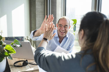 Happy businessman and colleague giving high-five in office - UUF28505