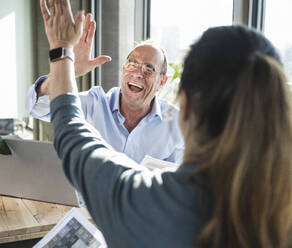 Happy mature businessman and colleague doing high-five in office - UUF28506