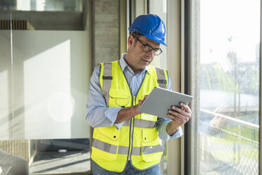 Mature engineer using tablet PC standing by window in office - UUF28523