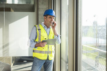 Mature engineer talking on smart phone looking through window - UUF28525