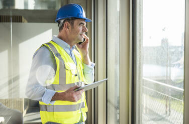 Smiling engineer with tablet PC talking on smart phone in office - UUF28527