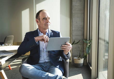 Nachdenklicher reifer Geschäftsmann sitzt mit Tablet-PC im Büro - UUF28532