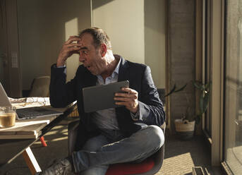 Geschockter Geschäftsmann mit Kopf in der Hand, der im Büro auf seinen Laptop schaut - UUF28539
