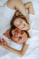 Lächelnder Mann, der mit seiner Tochter zu Hause auf dem Bett liegt - MDOF00866