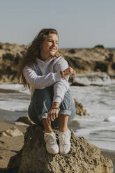 Lächelnde Frau verbringt ihre Freizeit auf einem Felsen sitzend - DMGF01085
