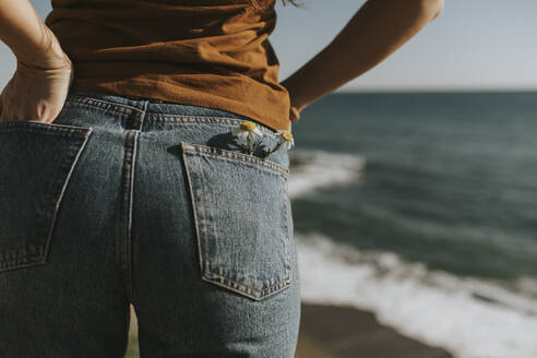 Blumen in der Gesäßtasche einer Jeans, die eine Frau am Strand trägt - DMGF01088