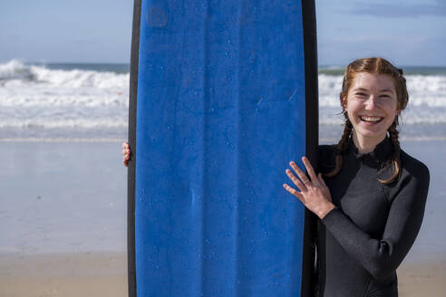 Glückliche junge Frau mit Surfbrett am Strand - LBF03789
