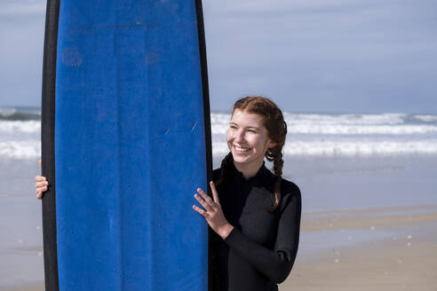 Lächelnde Frau mit Surfbrett am Strand stehend - LBF03790