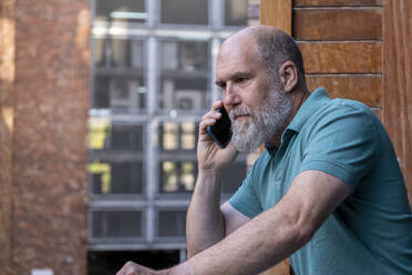 Älterer Geschäftsmann, der in einem Bürogebäude mit einem Smartphone telefoniert - LBF03793