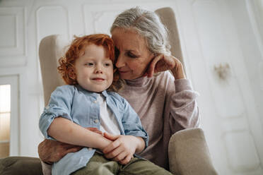 Grandmother and grandson sitting in armchair at home - MDOF00871