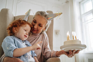 Senior woman with grandson holding birthday cake at home - MDOF00872
