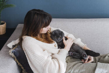 Woman reclining on sofa with cat at home - PNAF05043