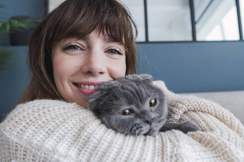 Lächelnde Frau umarmt Katze zu Hause - PNAF05050