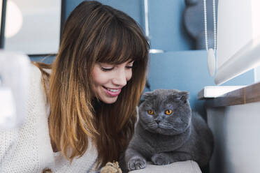 Lächelnde Frau verbringt ihre Freizeit mit ihrer Katze zu Hause - PNAF05053