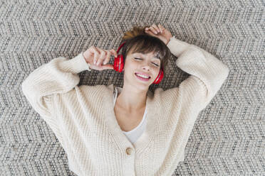 Carefree woman enjoying listening to music lying on floor at home - PNAF05061