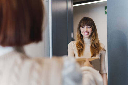 Smiling woman receiving package from delivery person at doorway - PNAF05071