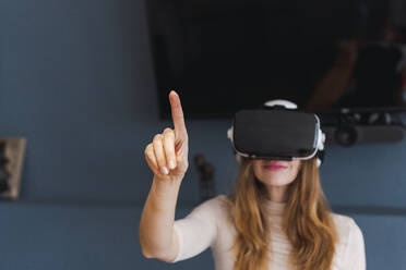 Woman wearing virtual reality headset gesturing at home - PNAF05080
