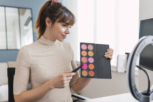 Influencer showing make-up palette on tutorial at home - PNAF05085