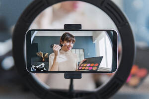 Smartphone-Bildschirm auf Ringlicht montiert mit Vlogger, der einen Make-up-Vlog filmt - PNAF05089