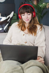 Frau mit drahtlosen Kopfhörern, die zu Hause auf ihren Laptop schaut - PNAF05100