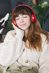 Woman with eyes closed listening music through wireless headphones at home - PNAF05101