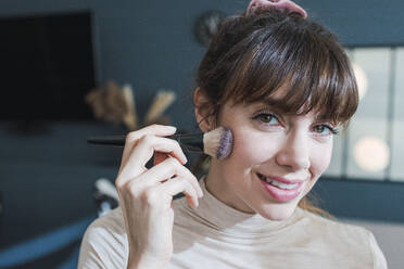 Smiling woman applying make-up using brush at home - PNAF05110