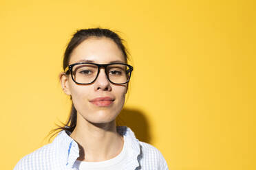 Lächelnde junge Frau mit Brille vor gelbem Hintergrund - MIKF00234