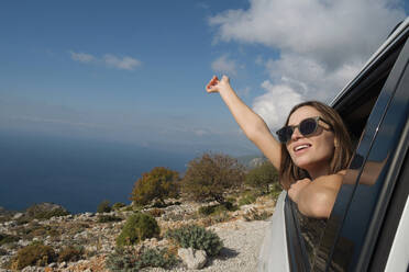 Smiling woman wearing sunglasses leaning out of car window at vacation - SYEF00313