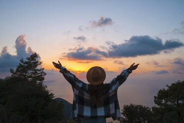 Woman with arms outstretched enjoying sunset on vacation - SYEF00320