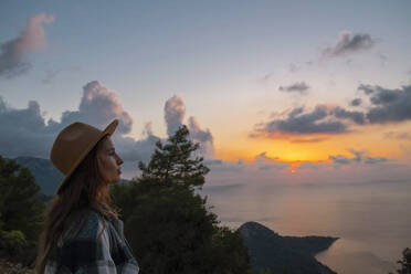 Woman wearing hat enjoying sunset at vacation - SYEF00321