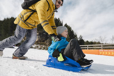 Father with son tobogganing on snow - ALKF00187