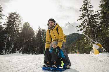 Glücklicher Vater und Sohn genießen das Schlittenfahren im Schnee - ALKF00189