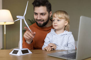 Happy father teaching about wind turbine to son at home - AAZF00161