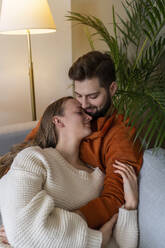 Mann umarmt Frau auf Sofa zu Hause - AAZF00168