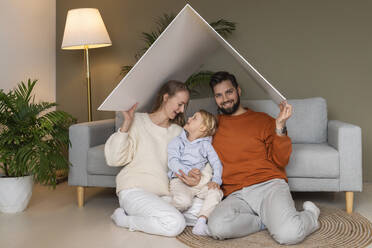 Lächelnder Vater und Mutter mit Sohn, die zu Hause unter einem Pappdach sitzen - AAZF00170