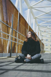 Frau sitzt im Schneidersitz auf einer Brücke an einem sonnigen Tag - SVCF00368