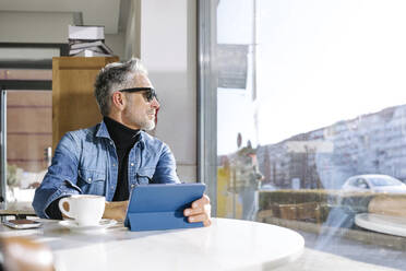 Businessman with tablet PC looking through window in cafe - JJF00693