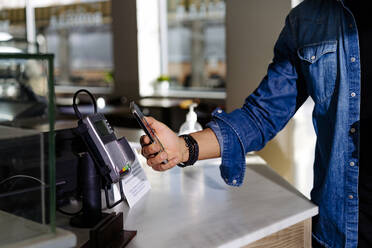 Mann beim Bezahlen mit dem Smartphone in einem Café - JJF00695