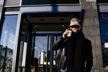 Mature businessman drinking coffee standing in front of building - JJF00697