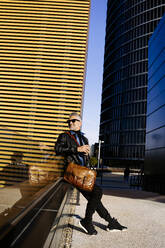 Smiling businessman sitting in front of buildings - JJF00699