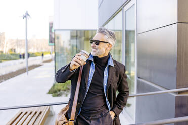 Happy businessman leaning with coffee cup on railing - JJF00706