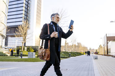 Businessman using tablet PC and walking on footpath - JJF00713