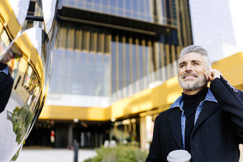 Smiling businessman talking on smart phone in front of building - JJF00733