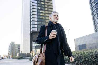 Lächelnder Geschäftsmann mit Kaffeetasse auf einem Fußweg - JJF00738