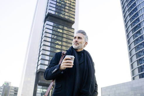Thoughtful businessman standing with disposable coffee cup - JJF00740