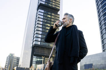 Businessman drinking coffee standing in front of building - JJF00741