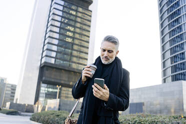 Businessman using smart phone in front of building - JJF00742